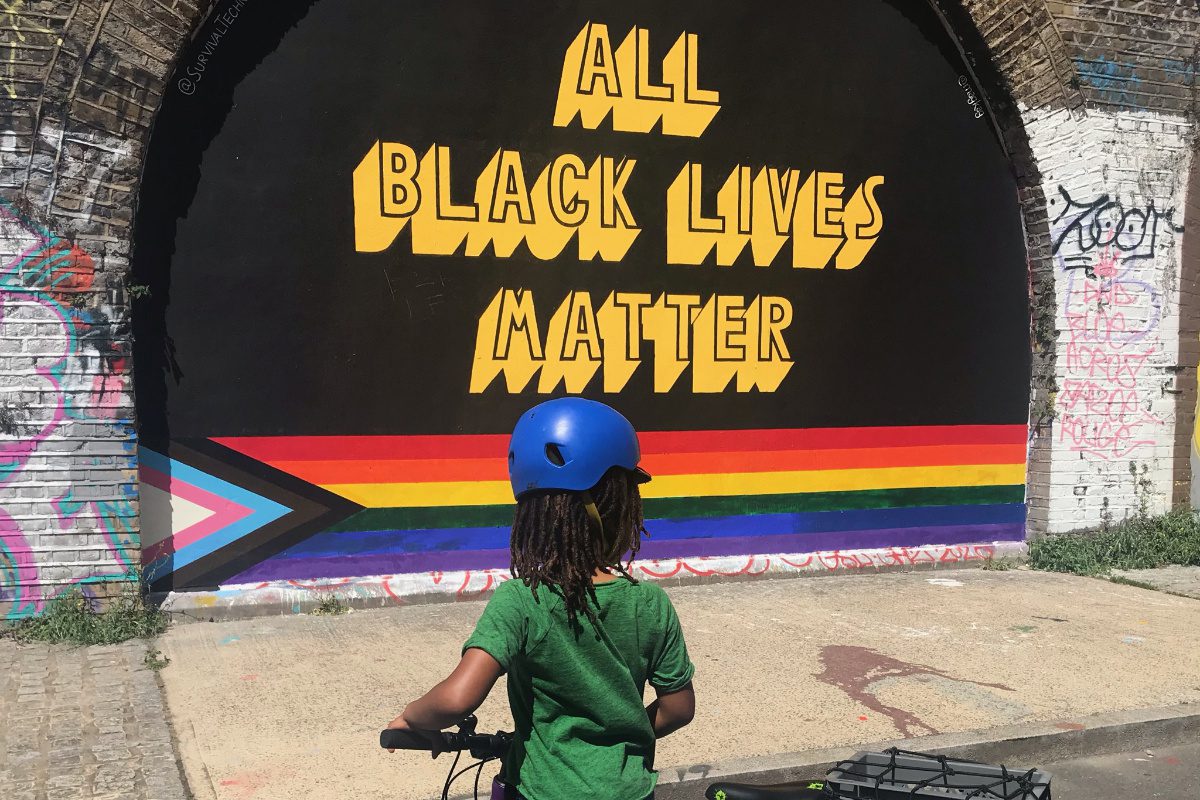 Young cyclist looking at All Black Lives Matter mural