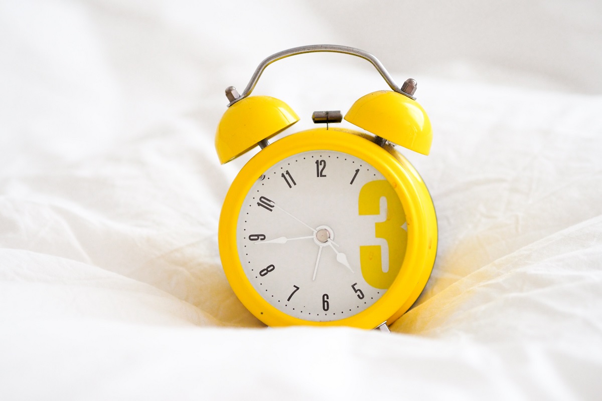 Yellow alarm clock on white duvet