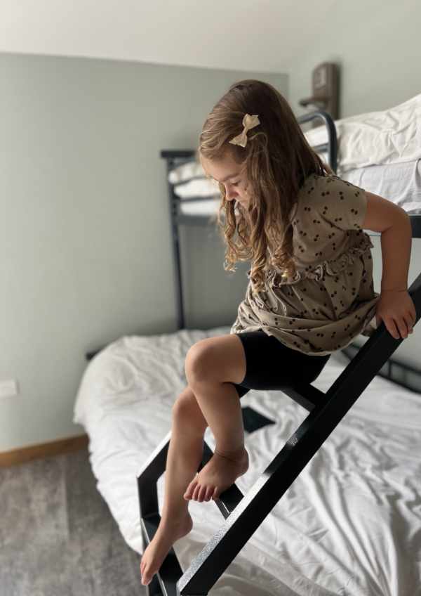 A young girl on the ladder of a bunk bed