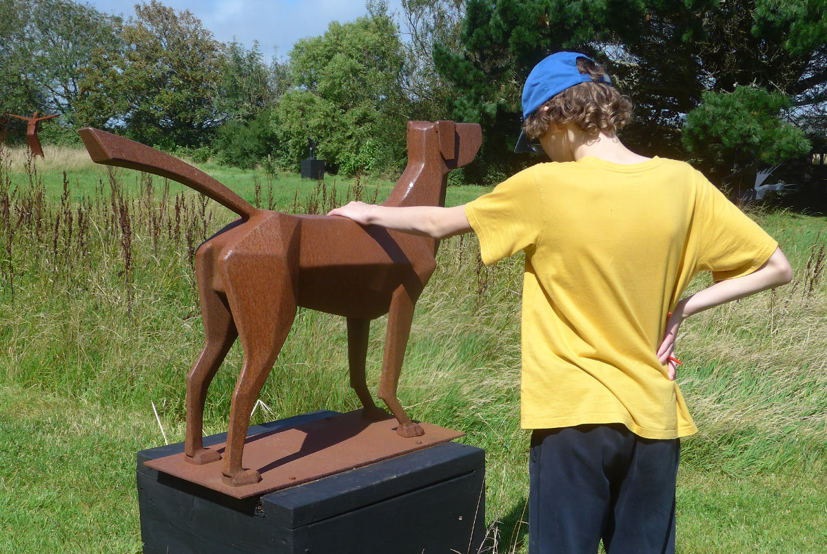 young boy petting a statue of a dog on a wooden plinth